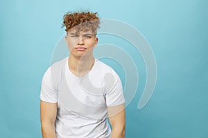 sad, gloomy young man with curly hair stands on a light blue background and looks into the camera, emotionally maning