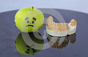 Sad green apple crying next to plaster model of lower teeth