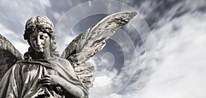 Sad guardian angel sculpture with open wings isolated with blurred white clouds dramatic sky. Sorrow angel sad expression sculptur photo