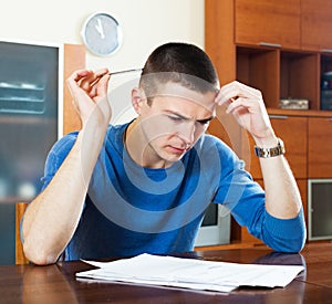 Sad guy fills out financial documents at table in home interior