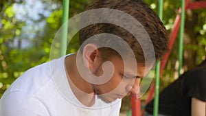 Sad guy and sad girl are sitting on a swing in the playground in the summer. Close up shot.