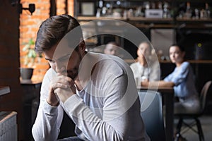 Sad guy sitting alone separately from other mates in cafe