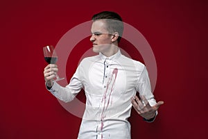 Sad guy in a white shirt spilled red wine on himself on a red background, an angry man put a stain of wine on his clothes