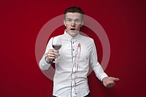 Sad guy in a white shirt spilled red wine on himself on a red background, an angry man put a stain of wine on his clothes