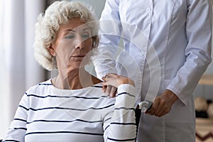 Sad handicapped woman sitting in wheelchair holding hand of caregiver