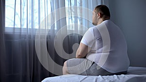 Sad heavy man sitting on bed at home, health problem, depression, insecurities