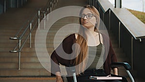 Sad helpless disabled young woman in front of the stairways in the wheelchair. inaccessible area