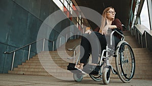 Sad helpless disabled young woman in front of the stairways in the wheelchair. inaccessible area