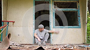 A sad homeless guy sits on the porch of an abandoned house. Bad neighborhood and poverty. The concept of vagrancy and homelessness