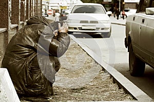 Sad homeless man sitting at the wall in city street