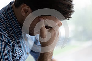 Sad hopeless young man sit alone indoor looks desperate