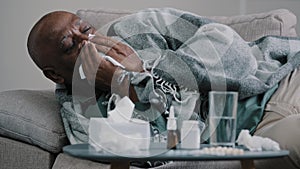 Sad ill elderly african american man lies on couch wrapped in warm blanket mature old grandpa coughing blowing runny
