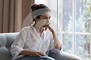 Sad Indian woman sit on armchair looks concerned, feels confused