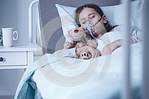 Sad kid with cystic fibrosis lying in a hospital bed with oxygen mask and plush toy photo