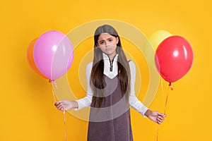 sad kid with party colorful balloons on yellow background