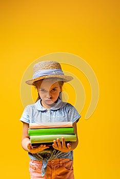 sad kid in straw hat holding books isolated on yellow.