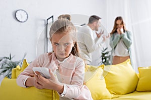 Sad kid using smartphone while parents