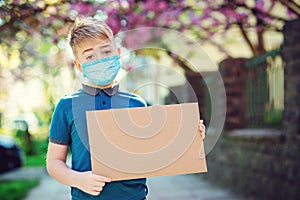 Sad kid wearing protective mask. Boy showing empty blank. Cute boy holding empty board outdoors. World global pandemic.