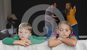 Sad kids leaning on sofa while parents arguing in background