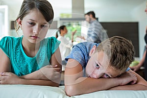 Sad kids leaning on sofa while parents arguing in background