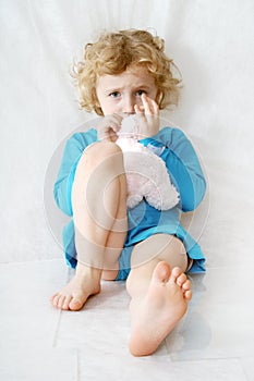 Sad little blonde curly sitting girl on the white with toy