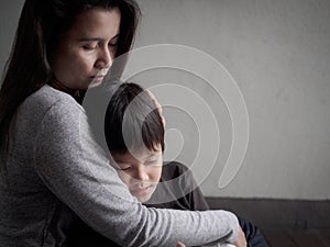 Sad little boy being hugged by his mother at home