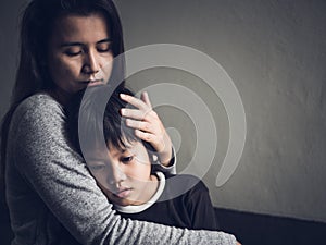 Sad little boy being hugged by his mother at home. photo