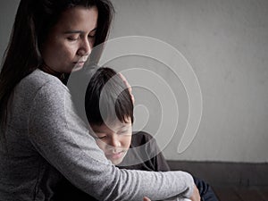 Sad little boy being hugged by his mother at home photo