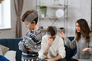 Sad little boy feels upset while his parents fighting at background. Mother and father quarrel. Family conflicts and