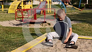 sad little boy with a fractured limb outdoors. a child with broken arm is sitting by the playground and touching plaster