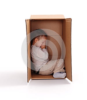 Sad little boy hiding in cardboard box