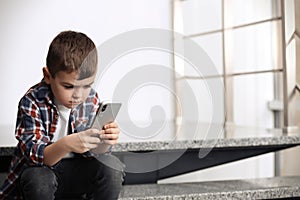 Sad little boy with mobile phone sitting on stairs
