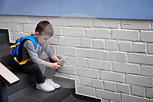 Sad little boy with mobile phone sitting on stairs