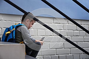 Sad little boy with mobile phone sitting on stairs