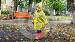 Sad little boy in raincoat walking in autumn park on rainy autumn day