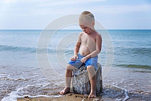 A sad little boy sits on the seashore with his head down on a sunny day. Resentment and misunderstanding