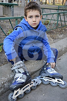 Sad little boy sits shod rollers on the curb.