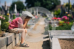 Sad little boy, sitting on a grave in a cemetery, feeling sad photo