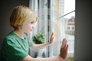 Sad little boy sitting near window and watching street. Post-traumatic disorder. Accommodation of grief. Experiencing loss. Fear.