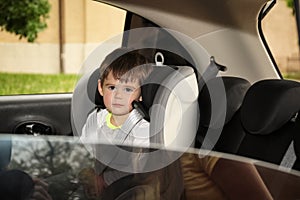 Sad little boy sitting in safety seat alone  inside car