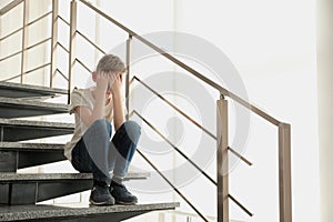 Sad little boy sitting on stairs indoors