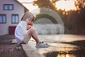 Sad little boy, sitting on the street in the rain, hugging his t