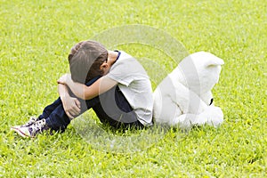 Sad little boy sitting with a teddy bear. Both turned away and lowered their heads. Sadness, fear, frustration, loneliness concept