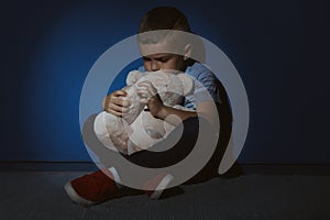 Sad little boy with teddy bear near wall. Domestic violence concept