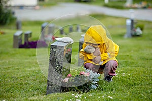 Sad little child, blond boy, standing in rain on cemetery, sad person, mourning