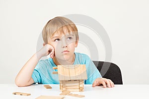 Sad little child dream aboout new home. Child builds with wooden blocks a small house