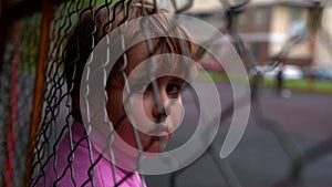 Sad little child is leaning on grid outdoors, abandoned lonely kid, homeless and street child