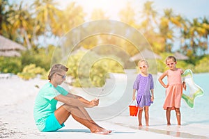 Sad little kids waiting for their dad working with laptop to swim and have fun on the beach