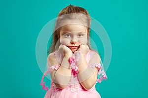 Sad little girl is bored, has a frustrated face, wears beautiful pink dress, portrait of child in bad mood on blue