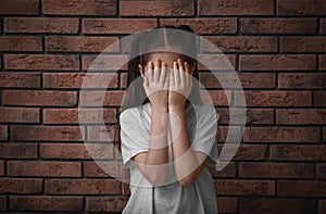 Sad little girl closing eyes with hands near wall. Child in danger